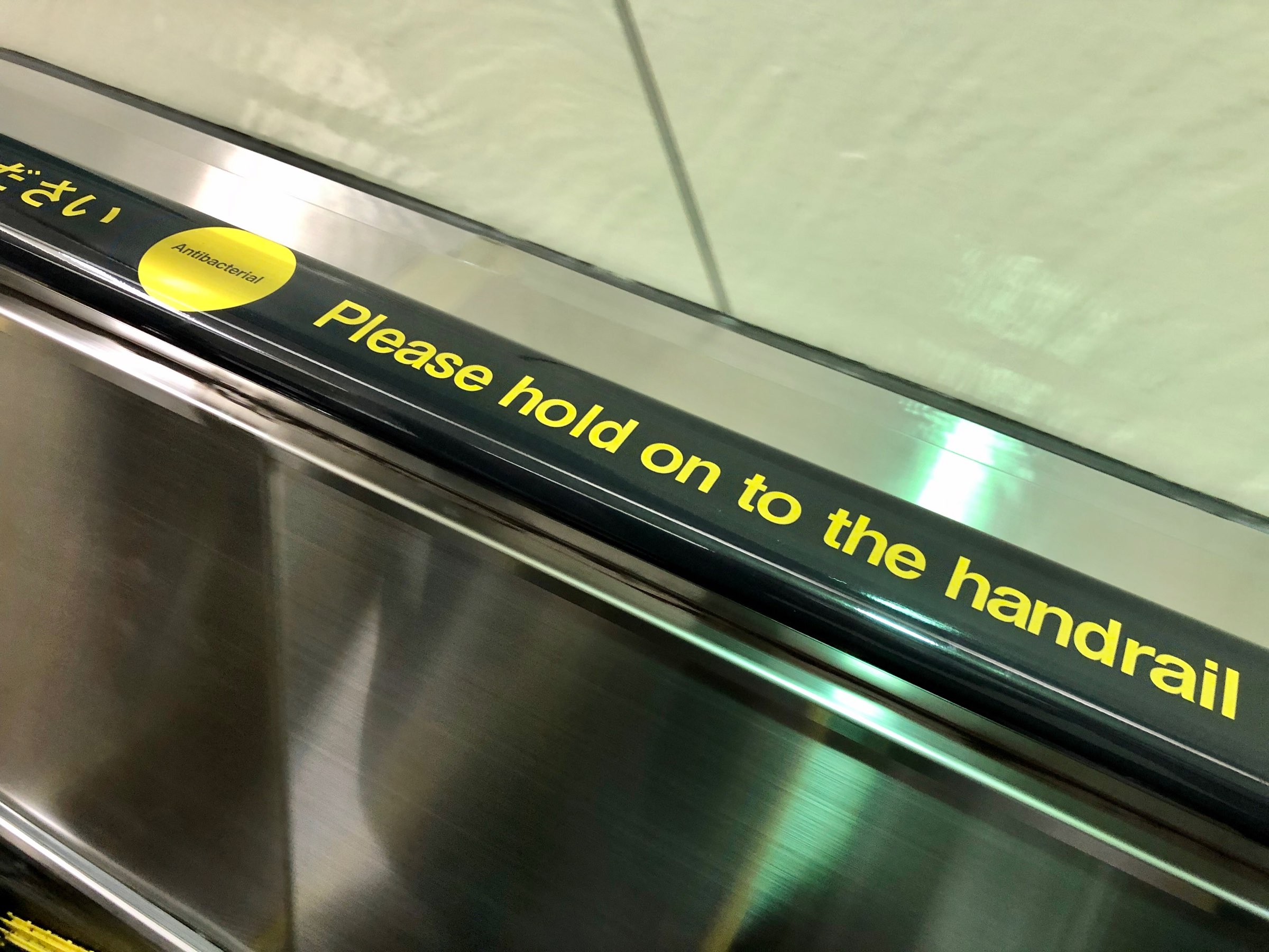 Escalator handrail with inscription, “Antibacterial - Please hold handrail”