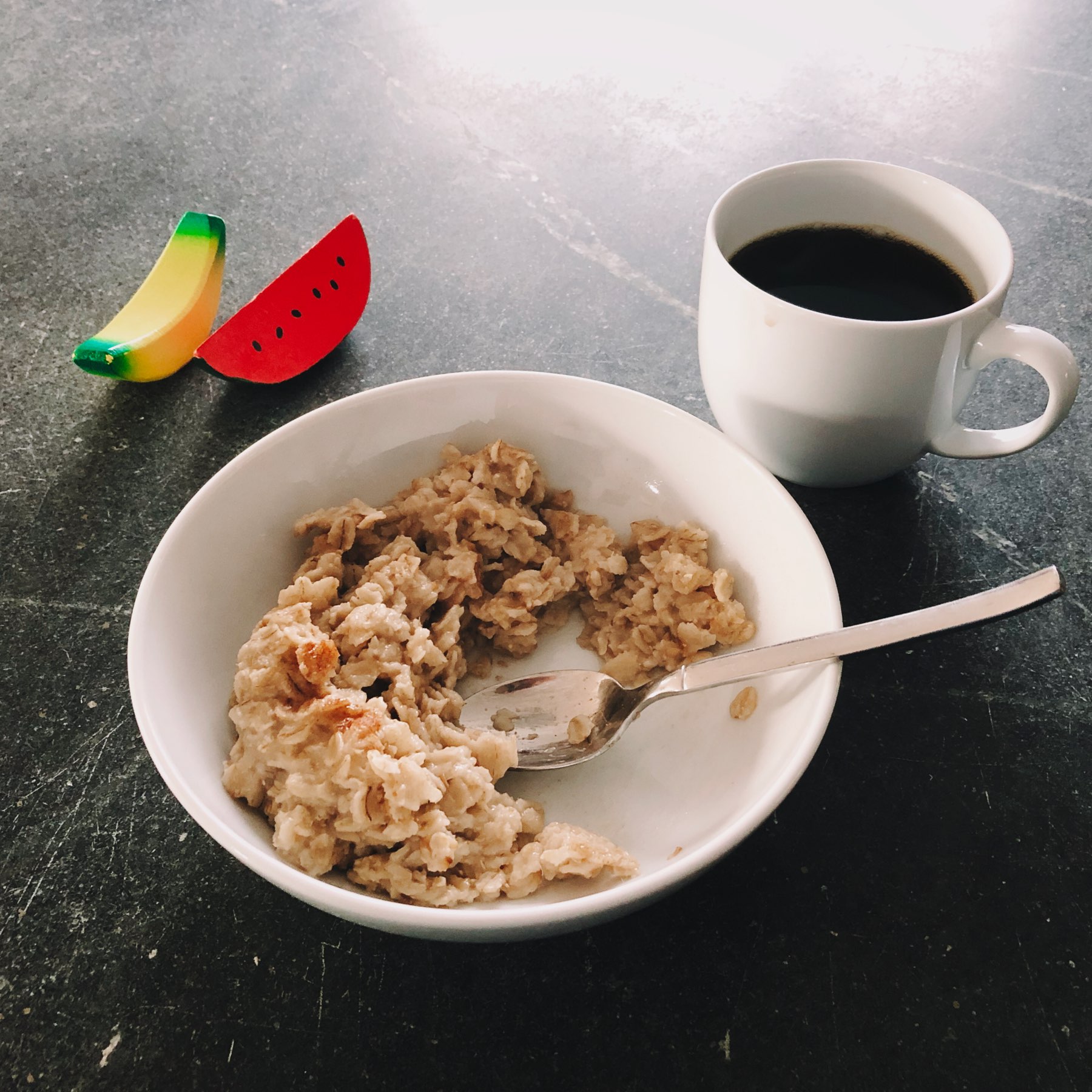Oatmeal and coffee, served with toy banana and watermelon.
